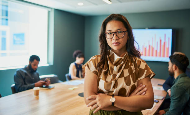 Confident Female Professional in Modern Office Environment Embracing Leadership and Success A Filipina woman wearing glasses and a stylish outfit stands confidently in a modern office, arms crossed, exuding confidence and
capability. In the background, her colleagues are engaged in a meeting, discussing ideas and strategies. The woman's determined expression and professional demeanor highlight her as a leader and a valuable asset to her team. legacy concept stock pictures, royalty-free photos & images