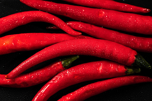 Red chili peppers shot from above on rustic wooden table. A chili peppers heap is in a small pan and three chili peppers are out placed directly on the table. Predominant colors are red and brown. Low key DSRL studio photo taken with Canon EOS 5D Mk II and Canon EF 100mm f/2.8L Macro IS USM