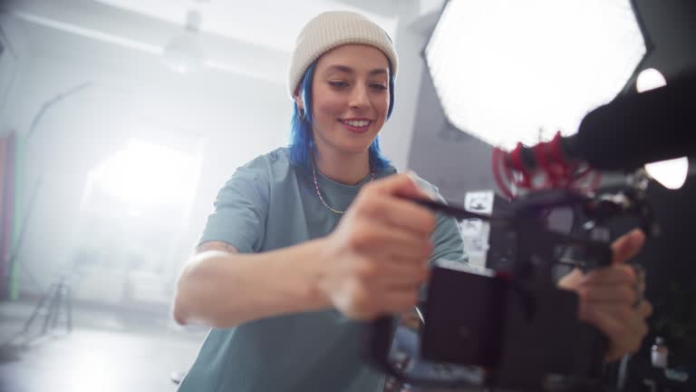 Young Female Director and Cinematographer Filming a Video in a Bright Studio, Giving Instructions to Model. New Generation of Filmmakers Using Smartphone to Shoot Budget-Friendly, High-Quality Project