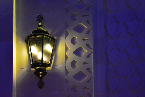Eastern style lantern on the wall with carved Arabic ornaments. Evening light.