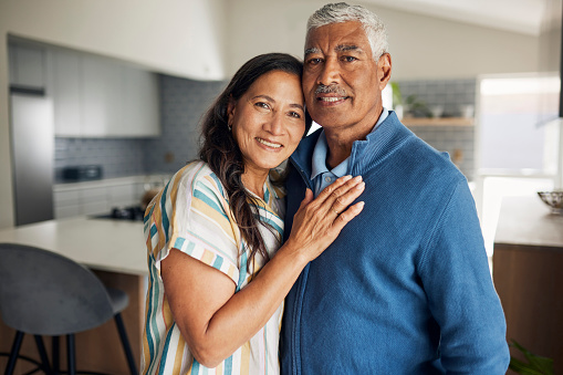 A happy retired couple is smiling and embracing in their kitchen.