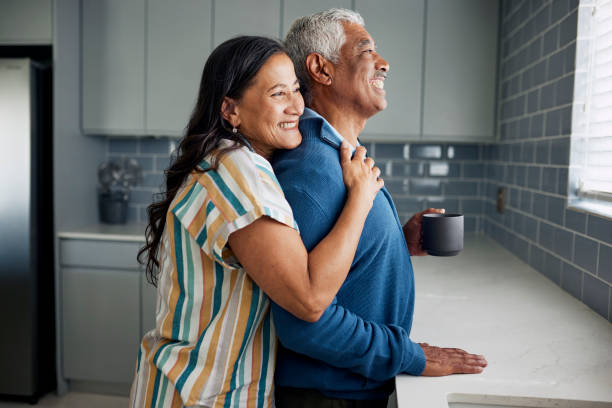 Happy Couple in Kitchen An elderly couple is drinking coffee and gazing out the kitchen window. legacy concept stock pictures, royalty-free photos & images
