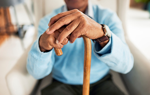 An elderly man is sitting in a chair with a cane in his hands.