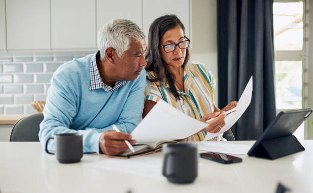Couple reviewing finances An older couple is sitting at their kitchen table reviewing financial documents. legal document stock pictures, royalty-free photos & images