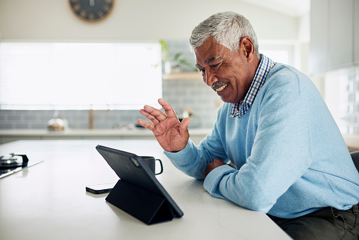 An elderly man smiles while video chatting on a tablet.