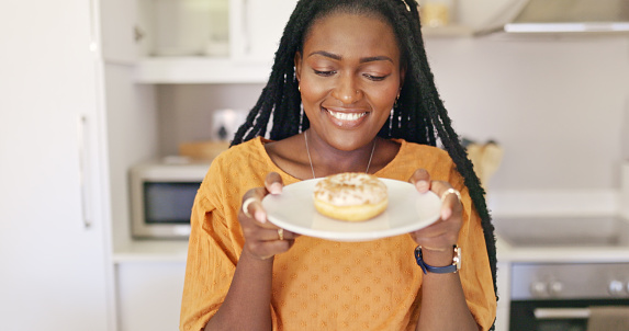 Attractive Young African American Woman Holding Plate With Donut And Smiling Away From Camera In Kitchen.