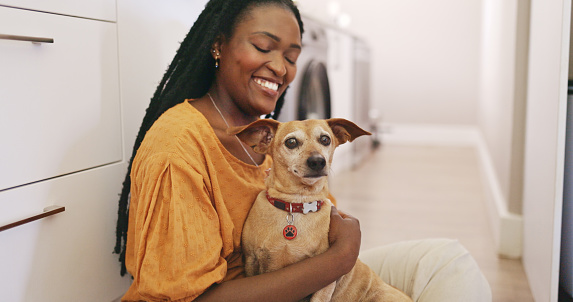 A joyful woman lovingly embraces a small, brown dog indoors, expressing their close bond.