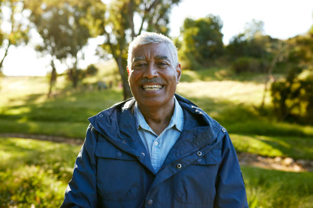 istock Smiling elderly man in a blue jacket standing in a park. 1887472031