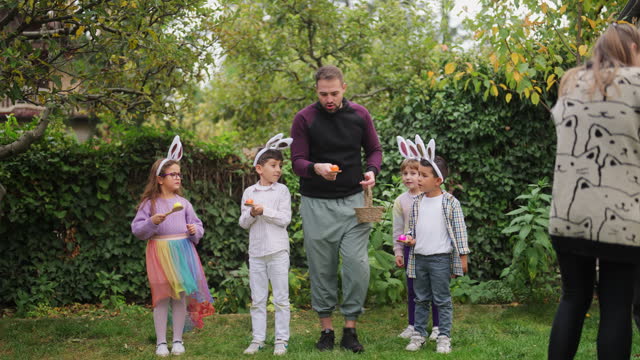 Young man explaining egg and spoon race to group of children outdoors