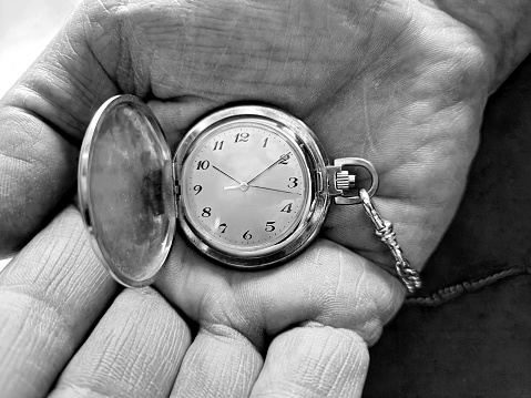 Close-up of a man's hand holding a pocket watch in monochrome