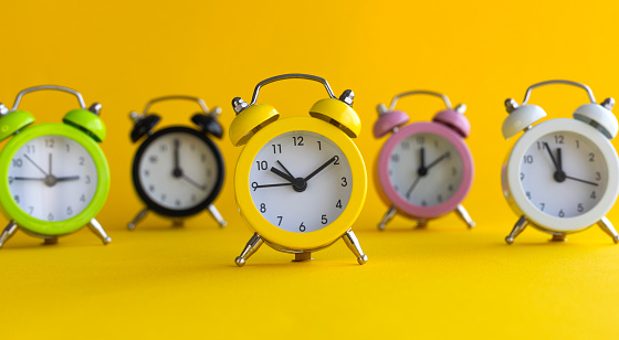Alarm clocks in different colors, yellow background.