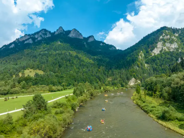 Tourist in wooden or pneumatic rafts and canoes approaching the Dunajec River Gorge in Pieniny Mountains in Poland. Trzy Korony (Three Crows) the highest summit in Pieniny in the background