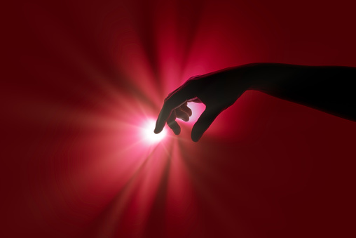 Silhouette of hand touching point of light on red background - Abstract image reflecting futuristic and cutting-edge technology.