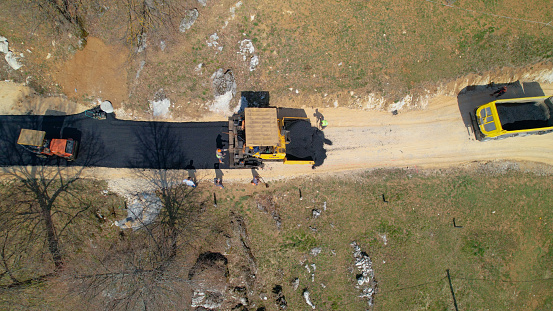 AERIAL TOP DOWN: Construction workers laying asphalt and freshly paved driveway. Builders preparing terrain for finishing paving the roadway in morning light. Roadworkers asphalt paving driveway.