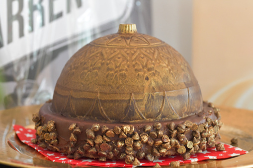 An ornate chocolate dome shaped desert, pudding, surround with golden sprinkles, regal, decedent dessert