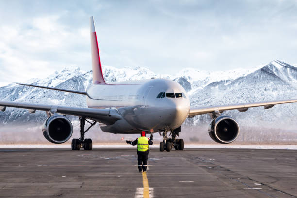 il marshaller dell'aeroporto incontra il jetliner del passeggero sullo sfondo delle alte montagne panoramiche - airfield mountain snow airport foto e immagini stock