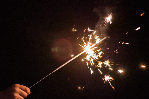 A sparkler being held by a young boy with its sparks firing brightly with the backdrop of a dark nights sky