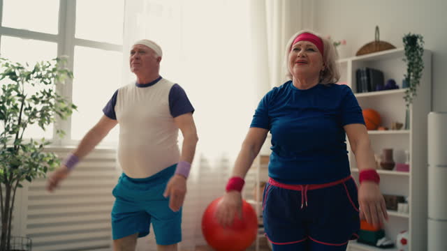 Positive senior couple doing squats together, exercising at home, fun activities