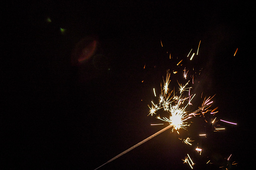 A flaming, ignited, sparking sparkler exploding sparkler with delicate strands of warm light with hints of gold and pink with the background of a dark nights sky