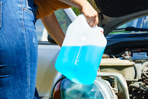 Woman pouring blue antifreeze liquid for auto windshield screen washing with bottle watering can.