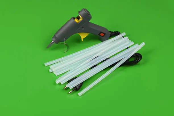 Electric hot glue gun with gluestick isolated on green background. High resolution photo. Full depth of field.