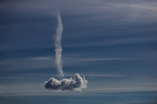 A white vaporous cloud in the shape of an aeroplane gliding through the bright blue sky