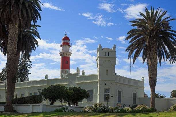 Red and white striped lighthouse, with a bright white stone old building and framed by a palm tree on either side