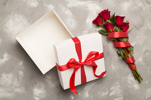 Open gift box with red roses on concrete background, top view