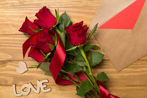 Red roses and letter on wooden background, top view