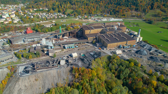 AERIAL: Industrial buildings and infrastructure for purpose of steel industry. Steel factory located by the river in picturesque valley surrounded with alpine landscape in colorful shades of autumn.