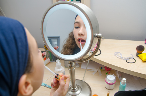 Teenage girl putting gloss on lips  in front of mirror