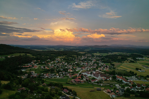 AERIAL: Dramatic and colourful summer storm clouds rolling above beautiful valley. Magnificent view of incoming evening thunderstorm glowing in sunset colors. Developing storm above hilly countryside.