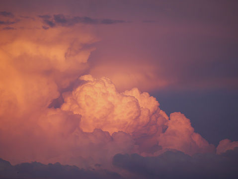 CLOSE UP: Dramatic clouds colored in vibrant pink and blue shades after sunset. Fluffy cumulonimbus cloud glowing in colors of summer sundown. Big rainstorm clouds developing on moody evening sky.
