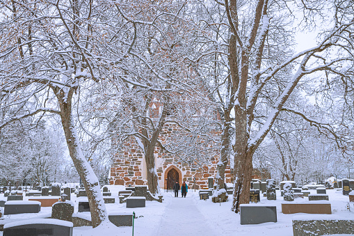 Lahti, Finland. December 25th, 2023. One of the oldest churches in Finland, originally catolic nowadays protestant covered by snow. Two persons visiting the cemetary.