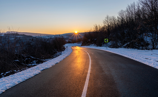 Empty asphalt road in rural landscape at sunset. Blue sky above the road. The sun's rays fall on the wet asphalt of the main road. Winter scene.