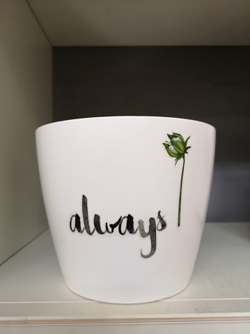 A white ceramic cup with a single red rose and the word 