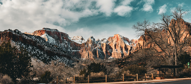 Behold the awe-inspiring beauty of Zion National Park's mountain ranges as our lens captures the grandeur of this pristine wilderness. Stretching as far as the eye can see, the rugged peaks rise majestically against the vast Utah sky, creating an iconic tableau of nature's magnificence.\n\nFrom the towering sandstone monoliths to the distant plateaus, the varied topography of Zion National Park unfolds in a breathtaking tapestry of earthy hues. The play of light and shadow accentuates the intricate details of the rock formations, casting a warm, golden glow during sunrise and sunset.\n\nThe camera skillfully navigates through the park, revealing the sheer scale and diversity of the mountain ranges. Deep canyons carve their way through the landscape, offering glimpses of hidden alcoves and narrow gorges that add an air of mystery to the scene. Verdant pockets of vegetation cling to the rocky slopes, creating a vivid contrast against the red and tan hues of the exposed terrain.\n\nThis footage is a visual ode to the natural wonders of Zion, perfect for nature documentaries, travel showcases, or any project seeking to convey the breathtaking beauty of mountain landscapes. Immerse your audience in the untamed splendor of Zion National Park—purchase your license today and bring the panoramic vistas of these majestic mountain ranges to life in your visual narratives.