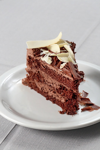 slice of chocolate cake with chocolate cream frosting and white chocolate shavings