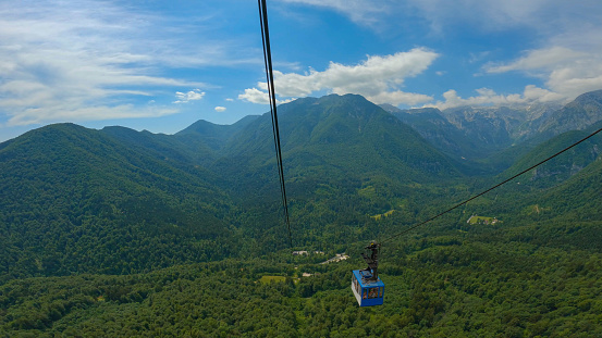 Gondola lift above lush green forest with stunning mountain views in springtime. Picturesque ride with cableway high above spring woods that connects valley and tourist destination in alpine mountains