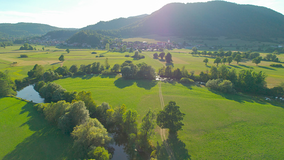 AERIAL: Wonderful view of vibrant green Planinsko Polje with winding river Unica. Picturesque countryside with grassland and slow-flowing river surrounded with lush forested hills on a summer day.