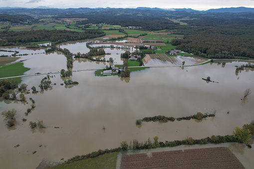 AERIAL: Heavy autumn rainfall caused the river to overflow in rural landscape. Flooded countryside after abundance of rain in autumn. Rising water spreading over grassy riverside, fields and woods.