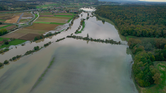 AERIAL: Rising muddy river overflowing its banks and flooding the countryside. Flooded landscape after abundance of rain in autumn season. Floodwater spreading over grassy riverside, fields and woods.