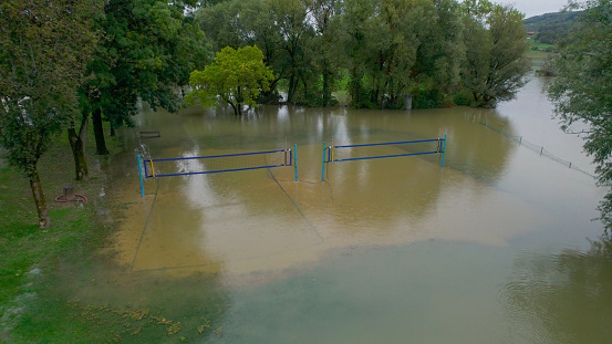 AERIAL: Volleyball court in park by the river is flooded with muddy flood water. Heavy autumn downpours filled the riverbed and caused river to overflow. Sports area in the public park is under water.