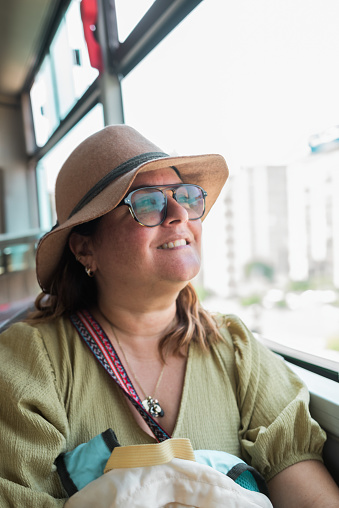 Portrait of a tourist sitting on the bus looking happily at the city through a window.