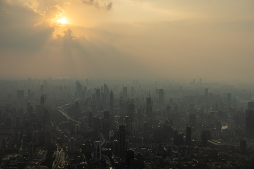 Aerial view of Shanghai at sunset, with sunrays piercing through the clouds and thick fog