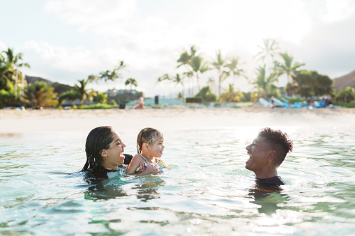 A cute three year old Eurasian girl has fun swimming in the ocean with her Hispanic aunty and Pacific Islander uncle while on a trip to Hawaii with her family.