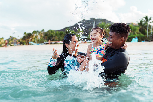 An adorable three year old Eurasian girl laughs while splashing in the ocean with her Hispanic aunty and Pacific Islander uncle.