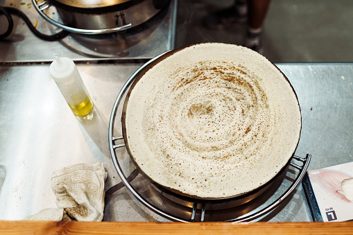 High angle view looking down at a dosa crepe being prepared by a chef in a casual restaurant serving Indian cuisine.