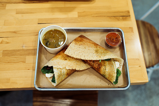 A silver tray with a south Indian meal of dosa and curry on restaurant counter waiting for customer to pick-up.