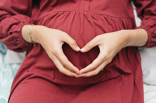 Asian Muslim pregnant woman holding her belly stomach creating love sign using hands